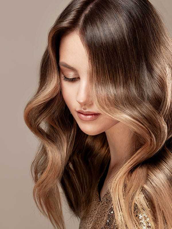 Woman with long, wavy hair gazing down, wearing a sparkly top.