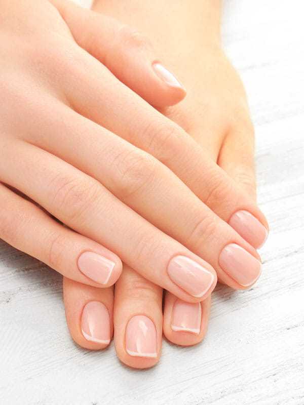 Manicured hands with pale pink nails on a white wooden surface.