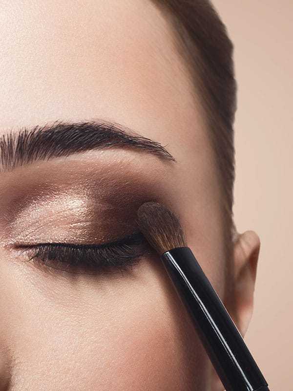Woman applying shimmery brown eyeshadow with a makeup brush.