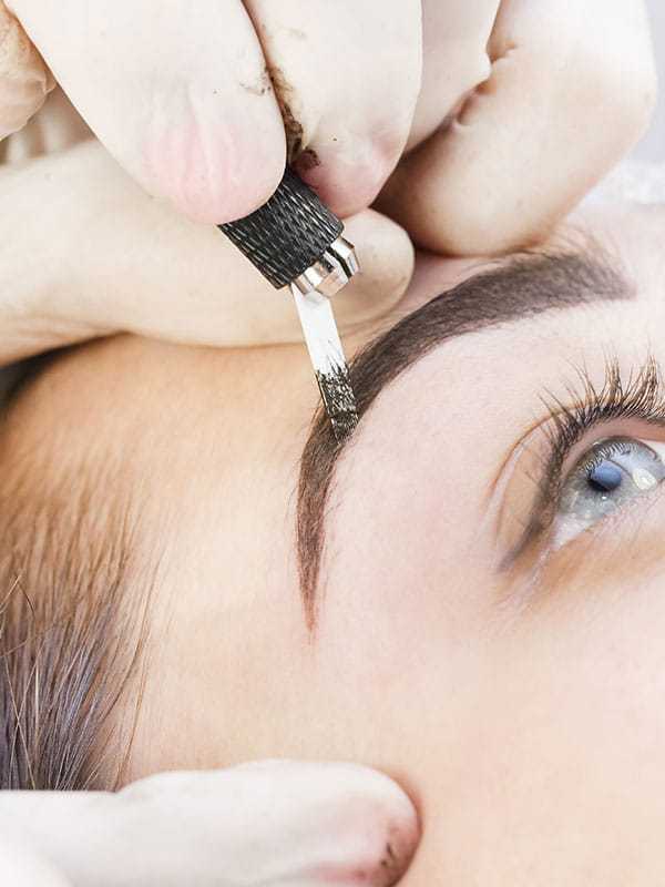 Eyebrow microblading procedure in progress on a woman's face.